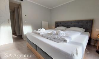 A modern bedroom with a large bed and fresh towels. The walls are light, and the room feels inviting.