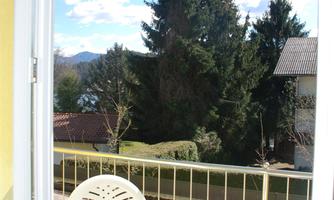 A cozy balcony with a small table and two chairs. In the background, there are trees and a blue sky.