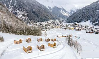 A picturesque winter village in the mountains, surrounded by snow-covered forest trees. Wooden cabins are harmoniously grouped in the snowy landscape.