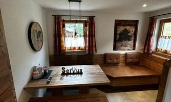 A cozy room with a wooden bench and a dining table. The windows are adorned with curtains and there are some decorative elements on the walls.
