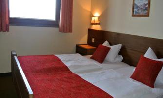 A cozy room with a double bed and red pillows. The room has a window with curtains and pleasant lighting.