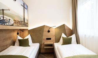 A modern room with two single beds and wooden paneling. The walls are decorated with a beautiful mountain landscape, and the light is warm and inviting.