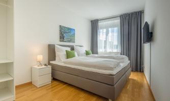 A bright bedroom with two beds and wooden flooring. A television and a nightstand complement the modern decor.