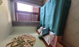 A cozy bedroom with two beds and colorful pillows. Large windows let in plenty of daylight.