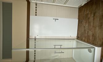 A modern bathroom with a clear shower cabin and a white door. The walls are tiled in light colors and the floor has a wood look.