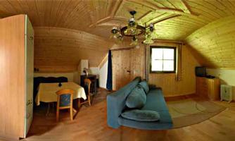 A cozy wooden apartment with a sleeping area and a living space. The furniture consists of a blue couch, a table, and a kitchenette.