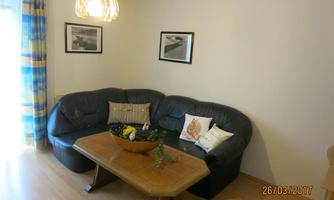 A cozy living room with a black sofa and a wooden table. Pictures hang on the walls, and a beautiful lampshade provides lighting.