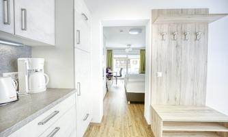 A modern kitchen with a clear view into a bright living and dining room. The entrance area features a wooden bench and coat hooks.