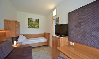 A simple room with two single beds and wooden furniture. A picture of a green landscape hangs on the wall.