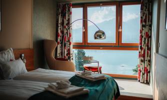 A stylish hotel room with two beds and windows that offer a view of a lake. Modern furniture and charming curtains create a cozy atmosphere.