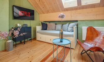 A cozy living space with a sofa, a table, and a decorative flower vase. On the wall, there is a television displaying the Netflix logo.