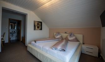 A modern bedroom with a large double bed and two pillows. A picture hangs on the wall, and a television is visible.