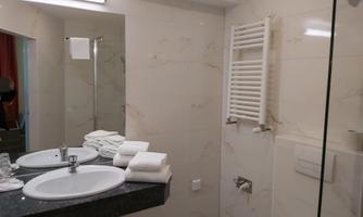 A modern bathroom with marbled walls, a sink, and fresh towels. In the background, a shower and a towel rack are visible.