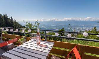 A cozy terrace with a view of the mountains and the valley. On the table are two wine glasses and a bottle of wine.