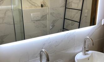 A modern bathroom with two sinks and a large mirror. The walls are designed with bright tiles and there is a glass shower.