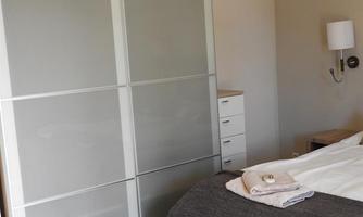 A modern bedroom with a large wardrobe and a comfortable bed. The walls are a light shade, giving the room a friendly and inviting feel.