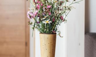 A beautiful bouquet of flowers in a bamboo vase sits on a wooden tray. Underneath lies a book that creates a cozy atmosphere.