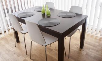 A modern dining table with four white chairs. There are placemats and two green vases on the table.