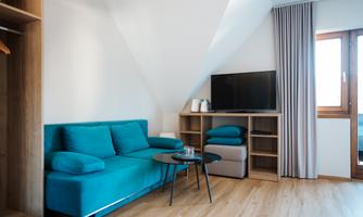A modern room with a turquoise sofa and a television. Large windows provide plenty of natural light.