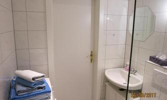 A modern bathroom with white tiles and a sink. On the left side are neatly folded towels.
