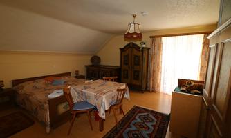 A cozy room with two beds and a table. Large windows let in plenty of light, and there is a wardrobe as well as a carpet.