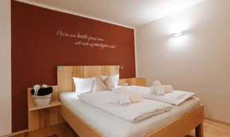 A cozy bedroom with a double bed and fresh towels. On the wall, there is an inspirational quote.