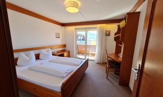 A modern hotel room with two single beds and wooden furniture. The room has a balcony with an outside view.