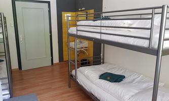 A simple room with two bunk beds and wooden floors. The walls are brightly colored and there is a door to another room.