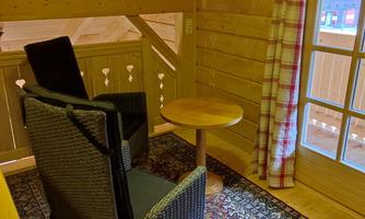 A cozy seating area in a wooden house. An armchair and a table are near a window with a view.
