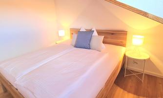 A cozy bedroom with a large bed and soft lighting. The wooden details give the room a warm atmosphere.