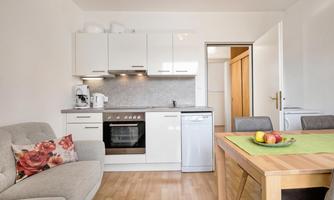 A modern kitchen with a dining table and two chairs. The decor is bright and inviting, with a cozy sofa.