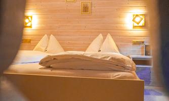 A cozy bedroom with wooden walls and a large bed setup. The light creates a warm and inviting atmosphere.