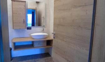 A modern bathroom with wooden shelves and a round sink. The room has bright walls and plenty of natural light.
