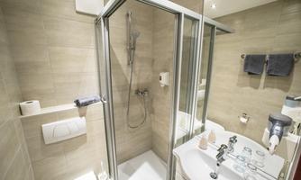 A modern bathroom with a glass shower and a sink. The walls are brightly tiled and there are towels and toilet paper nearby.