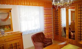 A cozy bedroom with wooden furniture and a large mirror. The windows are decorated with light curtains and the room has a warm, inviting atmosphere.