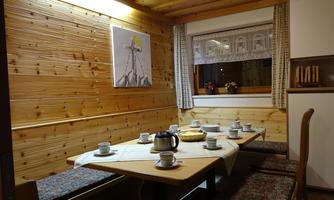 A cozy dining area with wooden walls and a large table. On the table, there are teapots and cups set for a coffee or tea gathering.