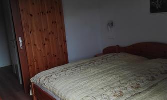 A cozy bedroom with a large bed and a wooden wardrobe. The walls are plain and the decoration is minimalistic.