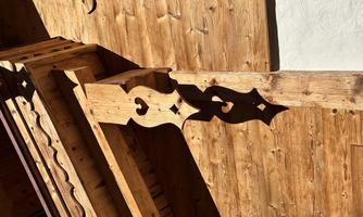 A wooden building with intricately carved beams and detailed work. The sun illuminates the wooden structure, highlighting the beauty of the architectural details.
