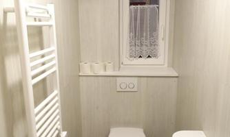 A modern bathroom with a toilet, towel radiator, and a small sink. The room has light-colored walls and a window with a curtain.
