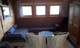 A cozy room with wooden walls and several windows. There is a seating area with sofas and a table as well as rattan furniture.