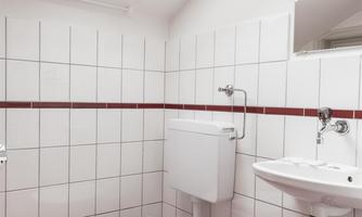 A small bathroom with white tiles and red accents. There is a toilet, a sink, and a window that lets in light.