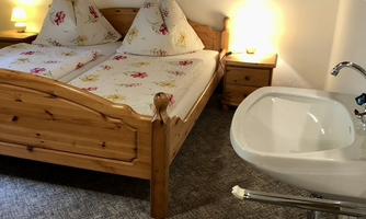 A cozy bedroom with a double bed and wooden details. Next to the bed there is a sink and soft lighting.