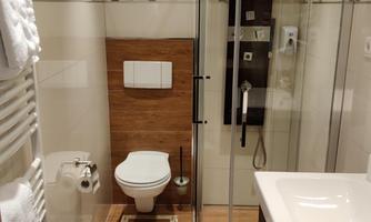 A modern bathroom with a separate shower and toilet. The walls are tiled in light colors and the floor has a wood effect.