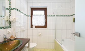 A modern bathroom with white tiles and a bathtub. The furnishings include a sink, a toilet, and a shower.