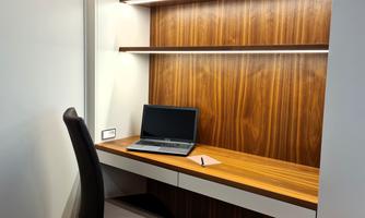 A modern workspace with a wooden shelf, a laptop, and a notepad on a stylish desk. The chair is comfortable, and the room feels tidy and inviting.