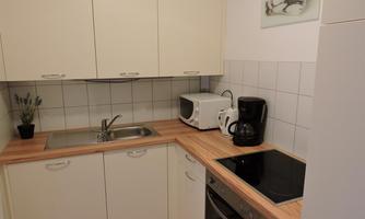 A modern kitchen with white cabinets and a wooden countertop. It is equipped with a stove, a microwave, and a kettle.