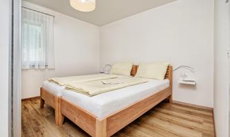 A cozy bedroom with a wooden double bed and light parquet flooring. The walls are white, and the room has a relaxed atmosphere.