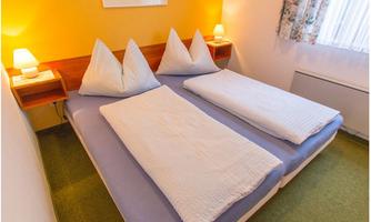 A cozy bedroom with two single beds and pillows. The walls are painted yellow, and there is soft lighting as well as a window with curtains.