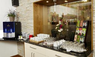 A kitchenette with a modern drink vending machine and a selection of tea types. Glasses and a decorative plant complete the picture.