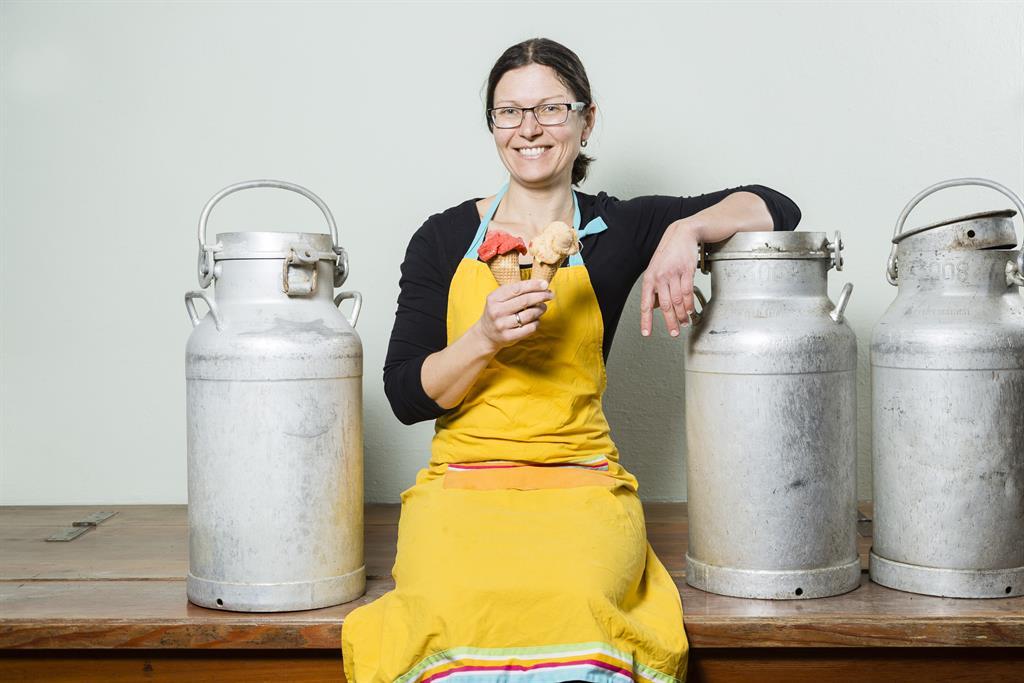 Frau mit Eiscreme-Tüten in der Hand, umgeben von Milchkrügen, in einem Geschäft in Österreich.